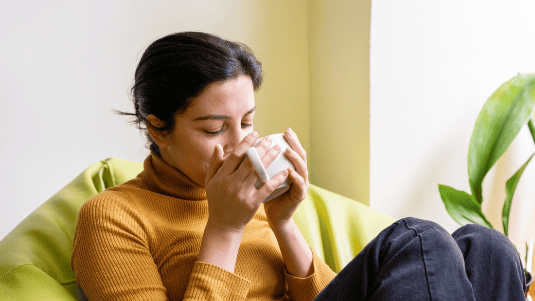 A comforting scene of a pregnant woman sitting on a sofa with a steaming cup of herbal tea, looking relaxed and content in soft, natural lighting.