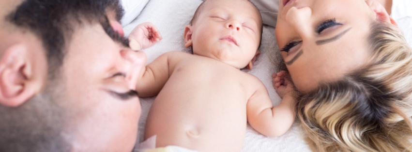 A newborn baby being gently cared for by parents, with baby care items in the background.