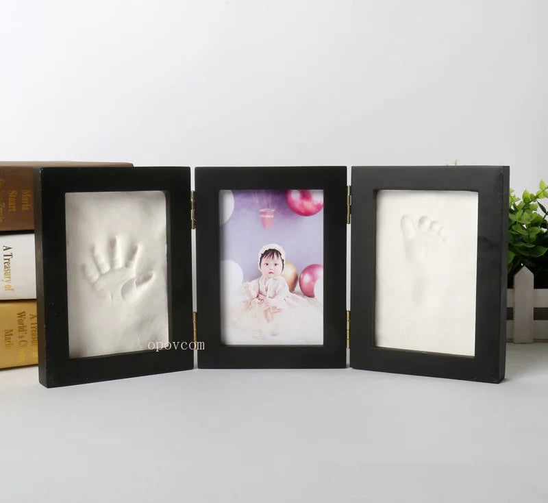 Black three-section photo frame with baby handprint and footprint on a white background.