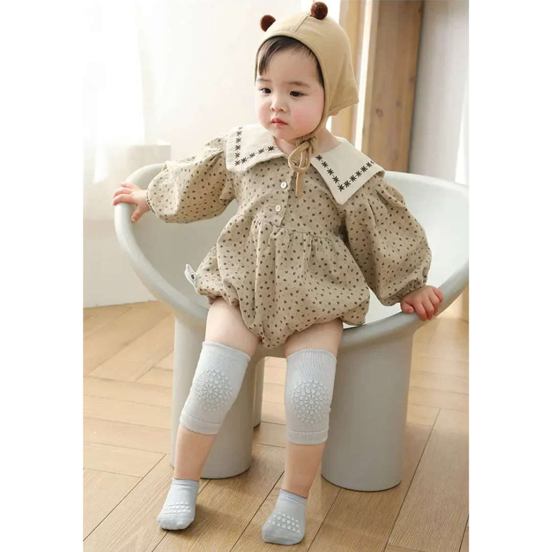 Child wearing a patterned outfit with a bonnet, standing on a white stool indoors.
