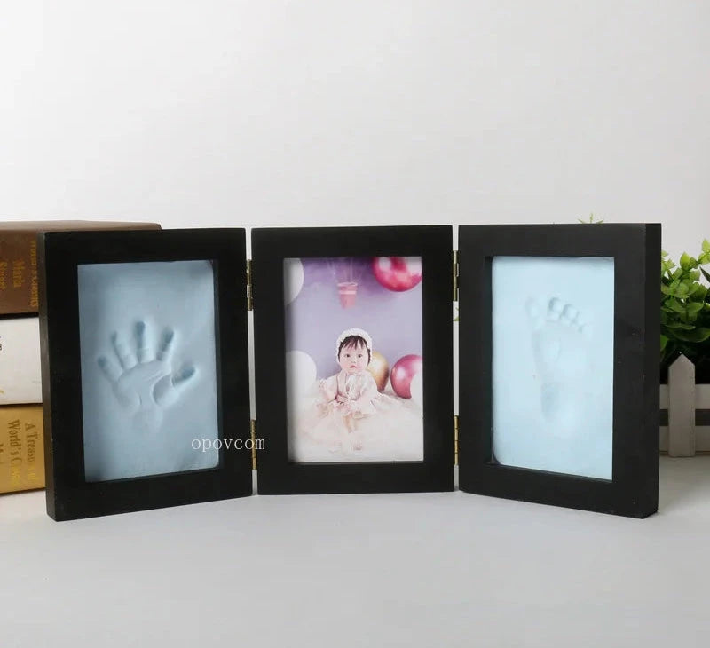 Black three-section photo frame with baby hand and footprints on a white background