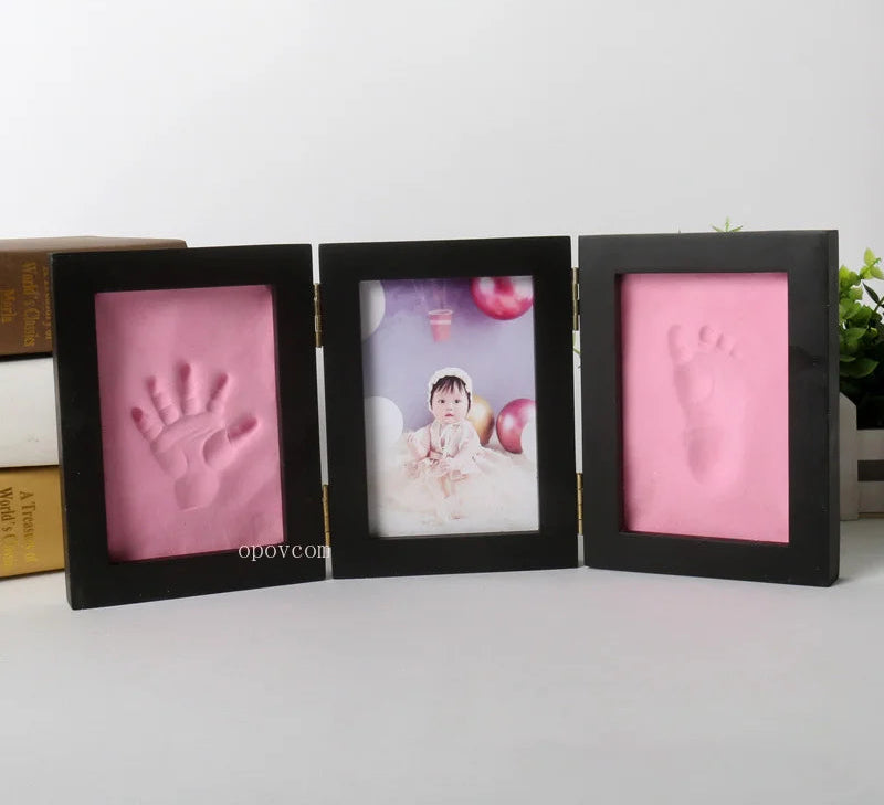 Three-section baby photo frame with pink clay for hand and foot impressions on a white background.