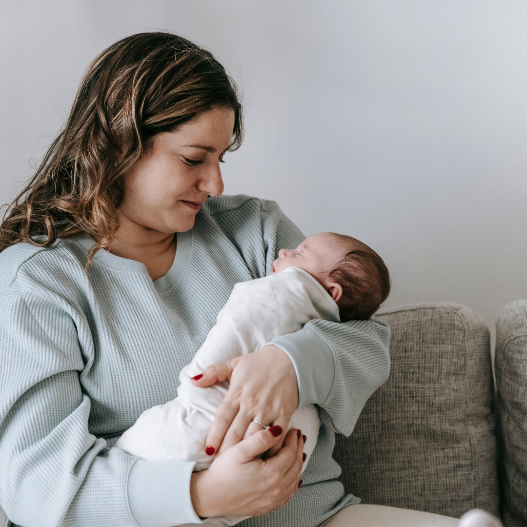 Woman holding a baby wrapped in a white blanket on a couch.