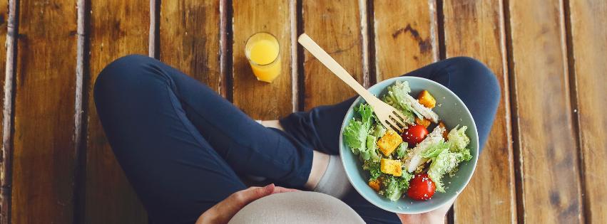 A colorful plate of healthy foods including fruits, vegetables, and grains, with a pregnant woman in the background.