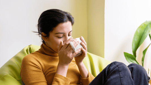 A comforting scene of a pregnant woman sitting on a sofa with a steaming cup of herbal tea, looking relaxed and content in soft, natural lighting.