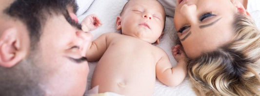 A newborn baby being gently cared for by parents, with baby care items in the background.