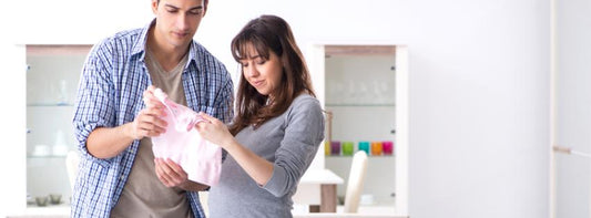 A nursery with a crib, baby clothes, and toys neatly arranged, with expectant parents in the background.