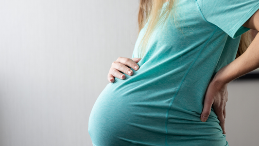 A pregnant woman holding her lower back in a home setting