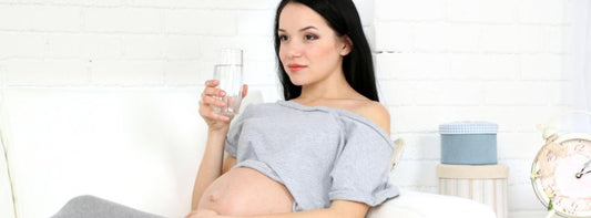 A pregnant woman sitting on a couch, looking comfortable and relaxed, with a glass of water and healthy snacks nearby.
