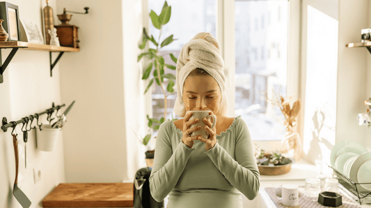 A serene morning scene with a pregnant woman sitting on a bed, sipping herbal tea, and smiling softly. Include soft, warm colours to create a calming and relatable image.