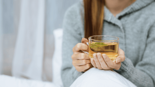 A serene scene of a pregnant woman sitting on a couch, sipping herbal tea, with a small table beside her holding crackers and a ginger root.