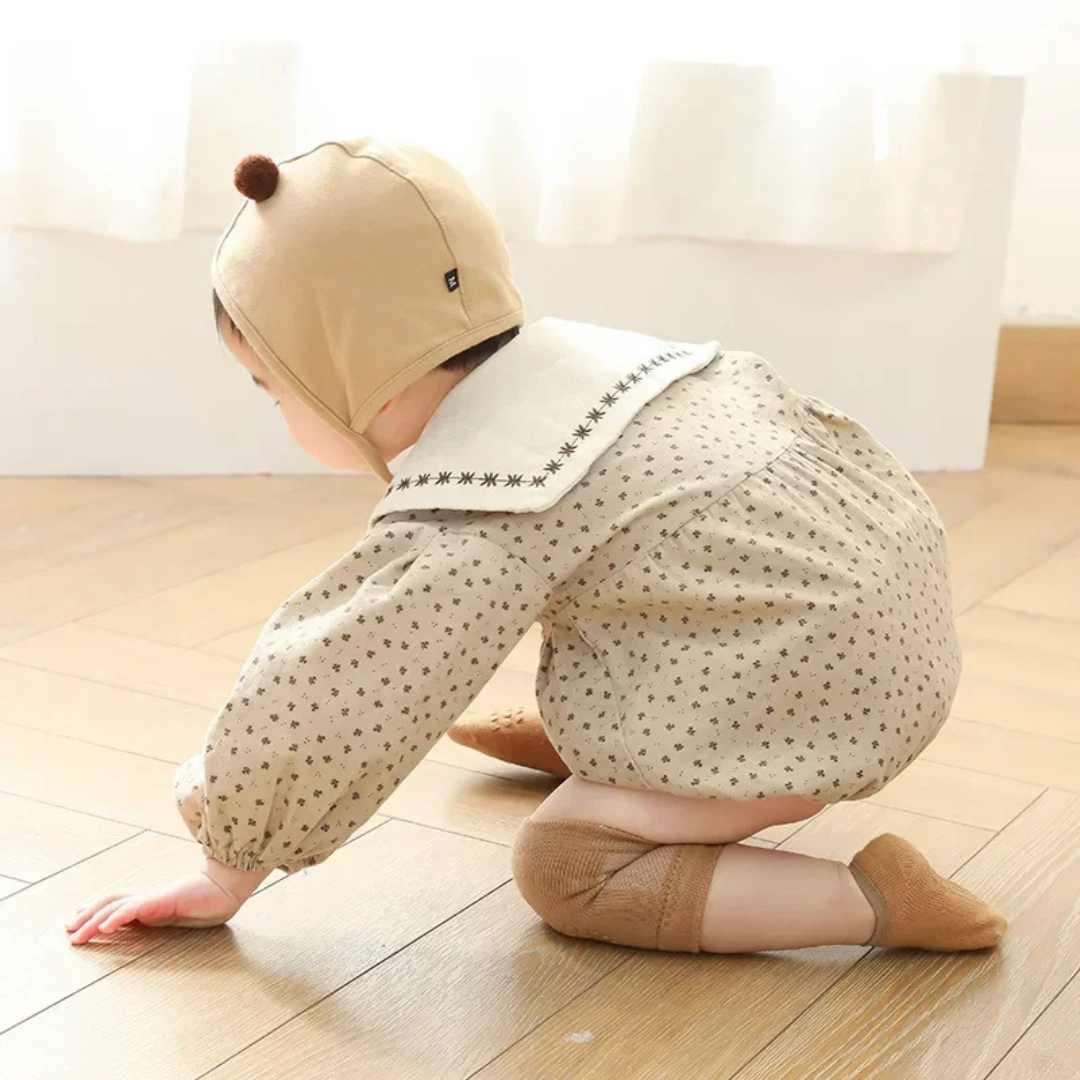 Child wearing a beige outfit with a hood and polka dot pants on a wooden floor.