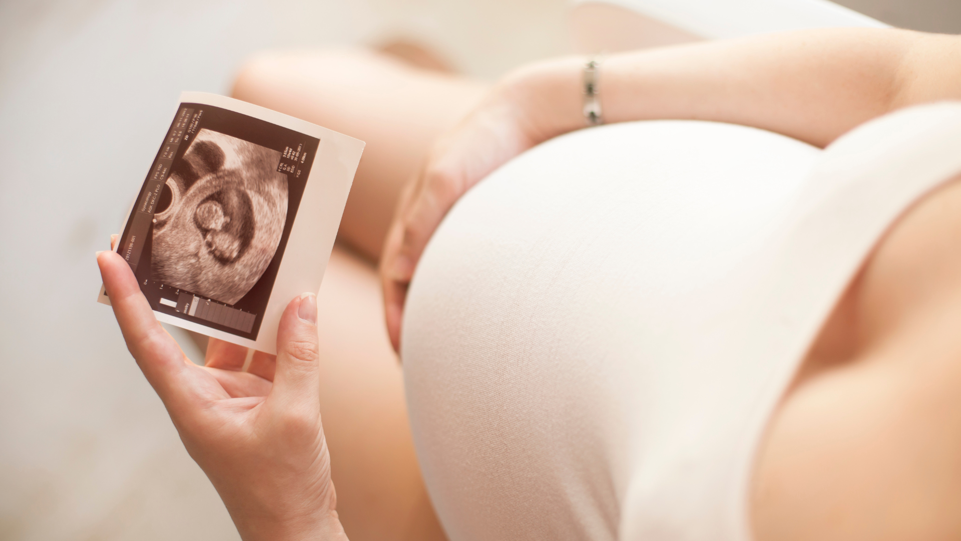 Pregnant woman holding her belly looking at an ultra scan of her baby