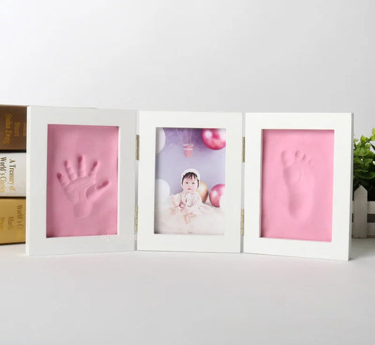 Three white frames with pink handprints and a photo of a baby on a light gray surface.
