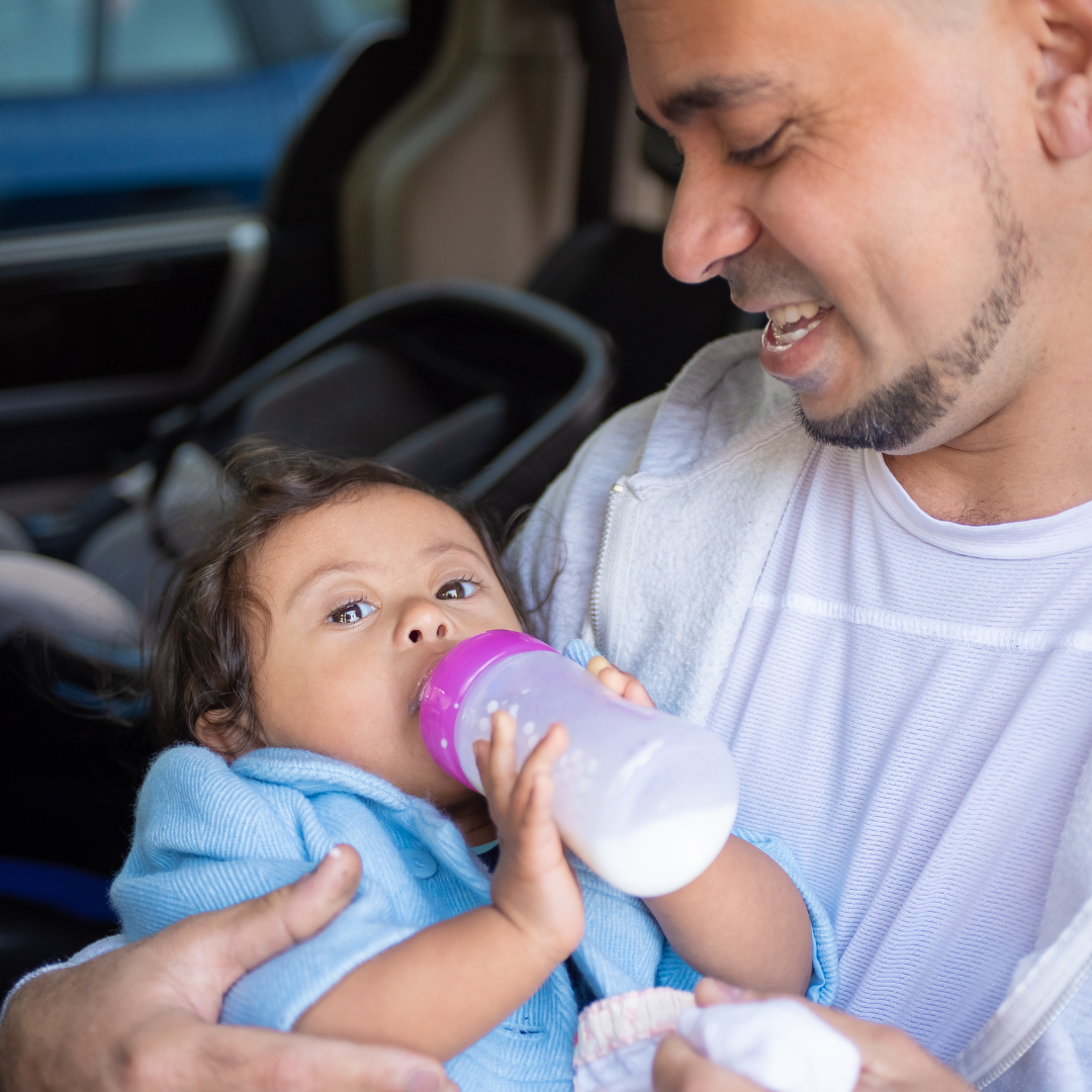 Man holding a baby and feeding them from a bottle inside a vehicle.