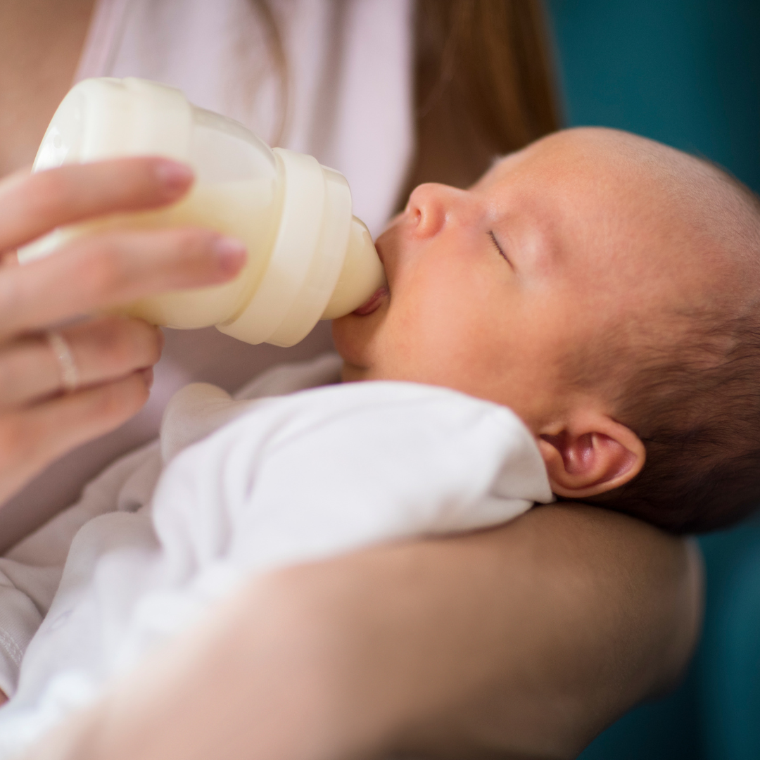 Baby being bottle-fed by a person with a blurred background