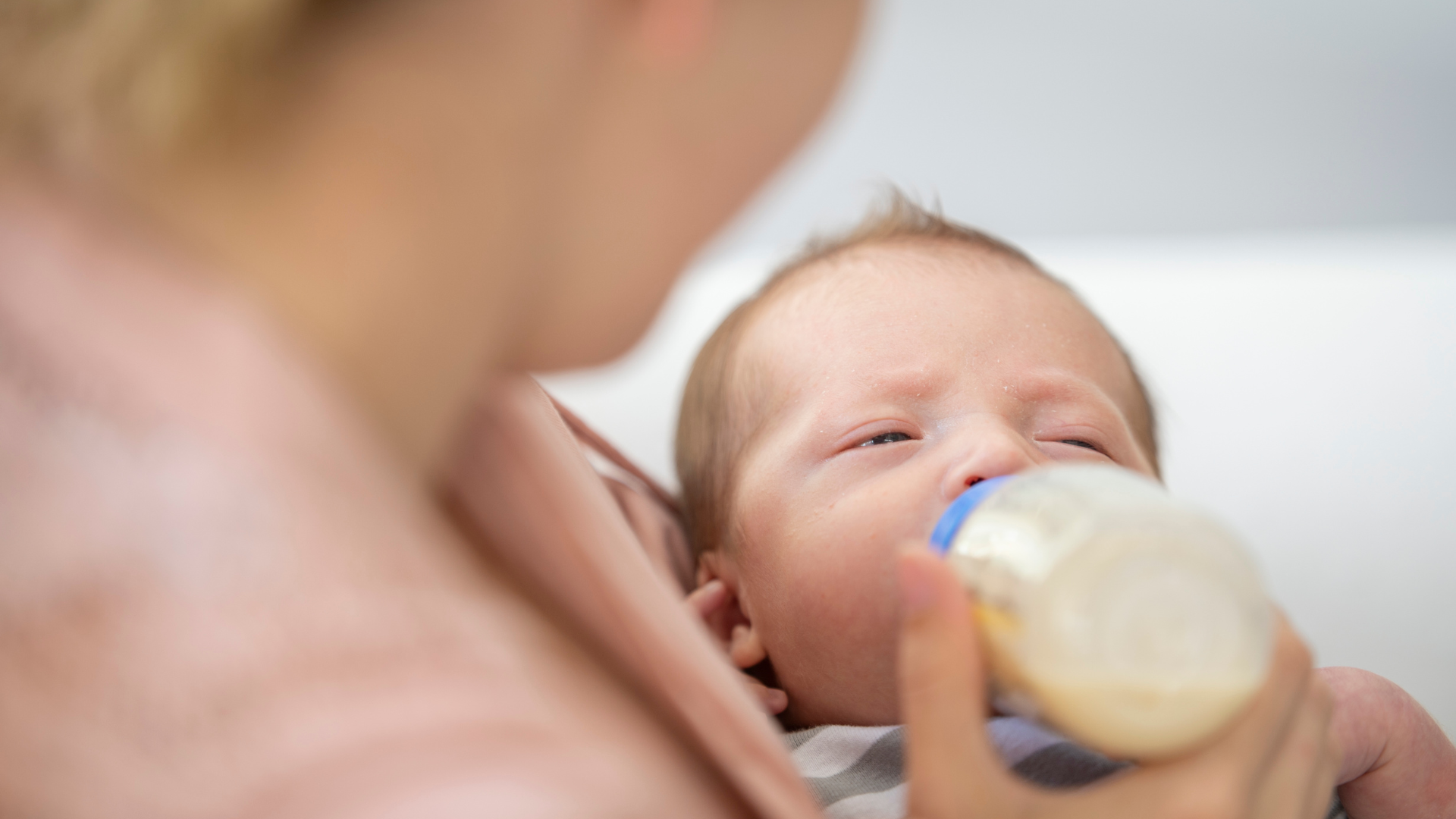 Baby being fed from a bottle with a blurred figure of a person holding the baby