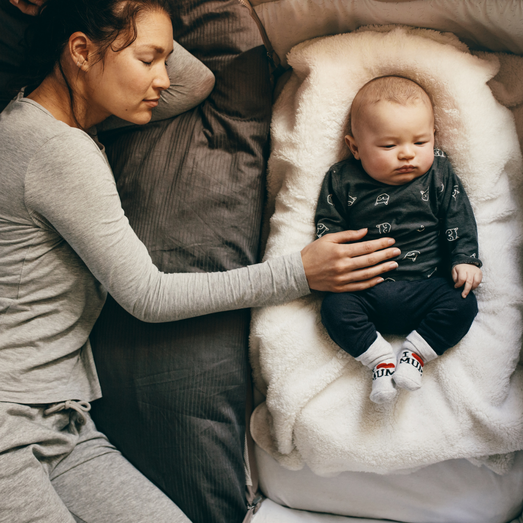 Woman lying on a bed with a baby in a crib next to her