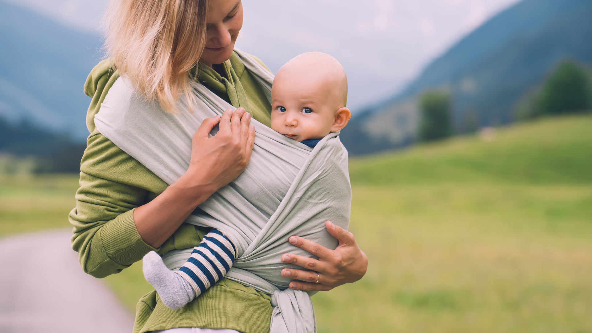 Woman holding a baby in a sling with a mountainous landscape in the background